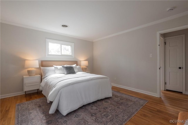 bedroom featuring ornamental molding, visible vents, baseboards, and wood finished floors