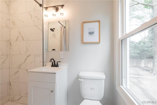 bathroom with toilet, a tile shower, and vanity