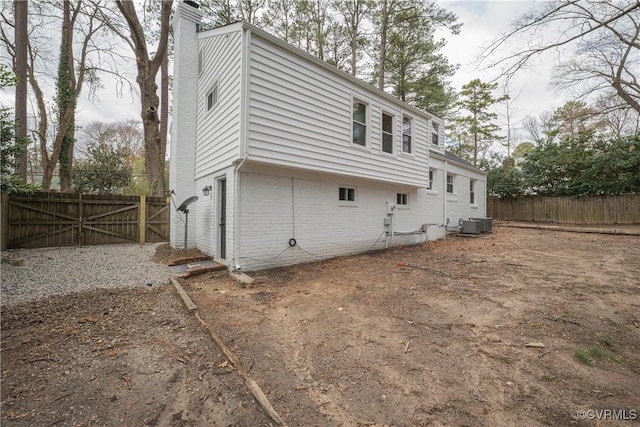 view of home's exterior featuring central AC unit, a chimney, fence, and brick siding