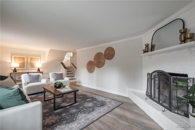 living area featuring ornamental molding, a brick fireplace, wood finished floors, baseboards, and stairs