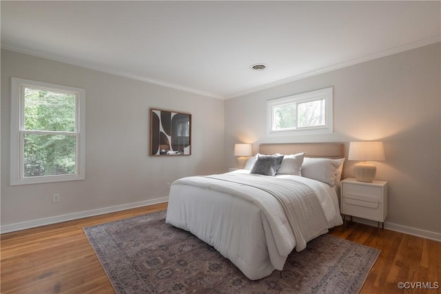 bedroom featuring ornamental molding, wood finished floors, visible vents, and baseboards