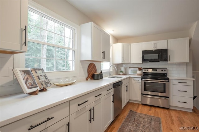 kitchen featuring a sink, light wood-style floors, white cabinets, appliances with stainless steel finishes, and tasteful backsplash