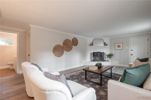 living room with a brick fireplace, crown molding, baseboards, and wood finished floors