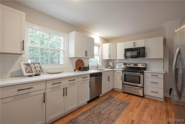 kitchen featuring stainless steel appliances, a sink, white cabinetry, light wood-style floors, and light countertops