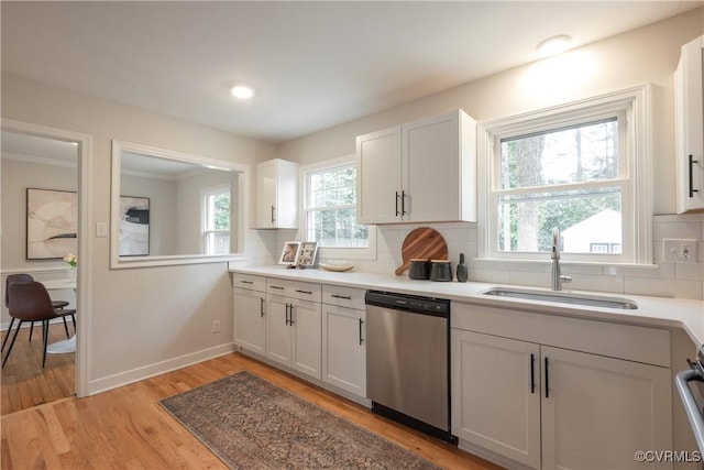 kitchen featuring decorative backsplash, stainless steel dishwasher, a sink, light wood-type flooring, and baseboards