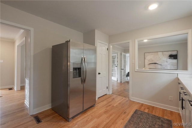 kitchen with crown molding, stainless steel refrigerator with ice dispenser, visible vents, light wood-type flooring, and baseboards