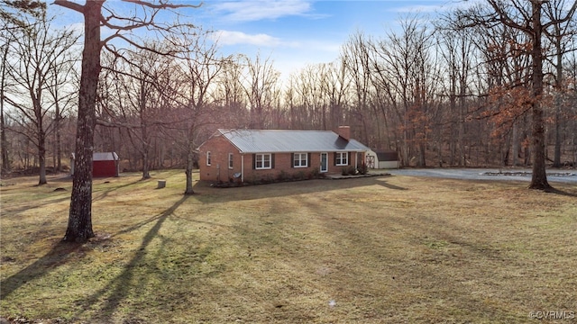 view of front of house featuring a chimney, metal roof, an outbuilding, a storage unit, and a front yard