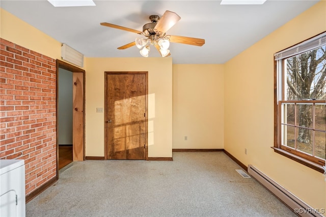 spare room with a skylight, washer / clothes dryer, a baseboard heating unit, brick wall, and baseboards