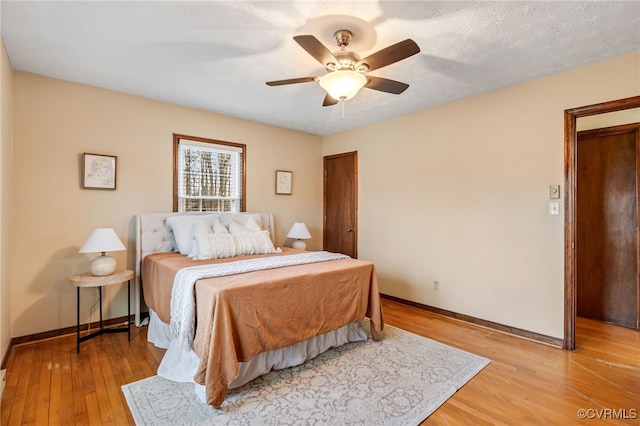 bedroom featuring light wood-type flooring, ceiling fan, a textured ceiling, and baseboards