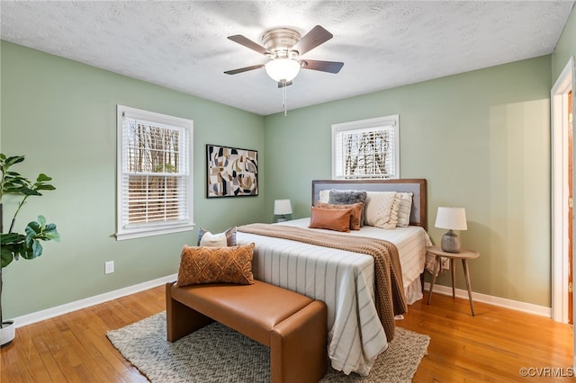 bedroom featuring light wood-style floors, ceiling fan, a textured ceiling, and baseboards