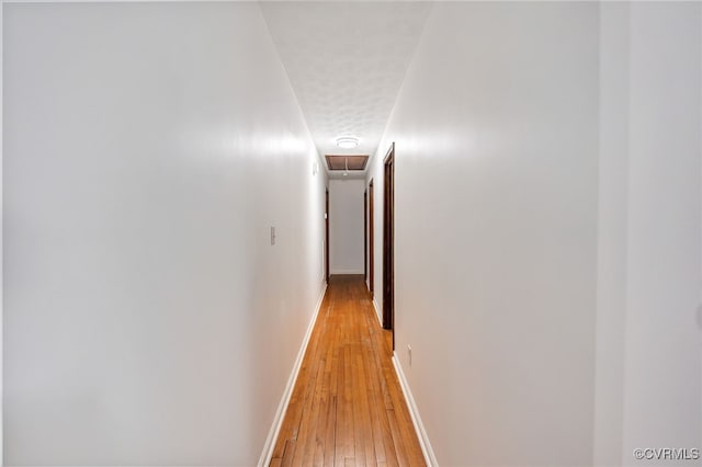 corridor featuring light wood finished floors, attic access, and baseboards