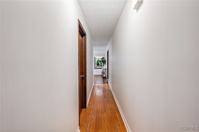 corridor with light wood-style floors, baseboards, and a textured ceiling