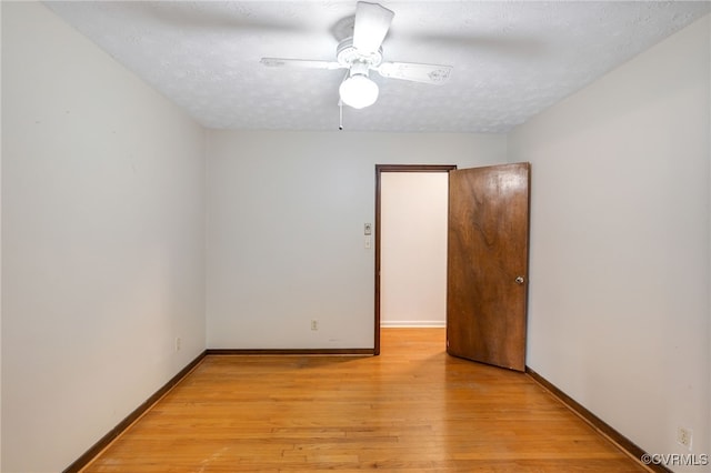 spare room with a textured ceiling, a ceiling fan, light wood-style flooring, and baseboards