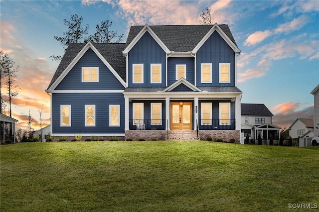 view of front facade with board and batten siding, a yard, a shingled roof, and a porch