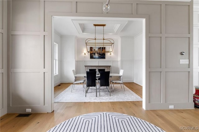 dining area featuring a notable chandelier, light wood-type flooring, a raised ceiling, and a decorative wall