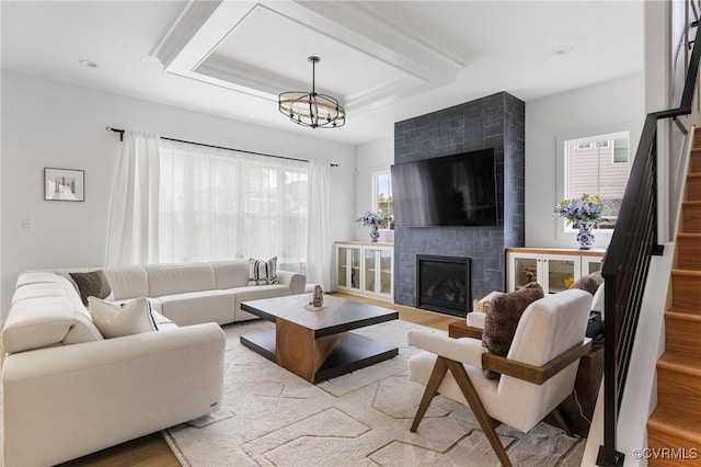 living area featuring a chandelier, a fireplace, wood finished floors, stairs, and a tray ceiling