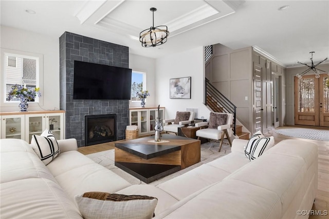 living room featuring a chandelier, wood finished floors, stairs, a tiled fireplace, and a raised ceiling