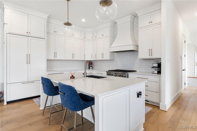 kitchen featuring light wood finished floors, a kitchen breakfast bar, custom exhaust hood, light countertops, and a sink