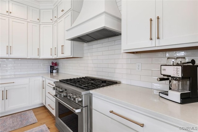 kitchen featuring white cabinetry, custom exhaust hood, light countertops, and high end stainless steel range