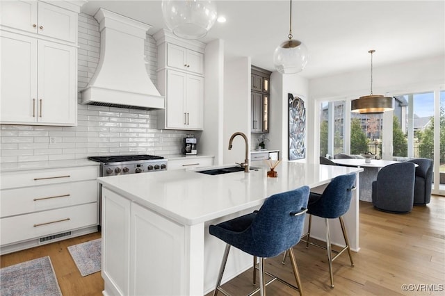 kitchen featuring premium range hood, a sink, visible vents, decorative backsplash, and light wood finished floors