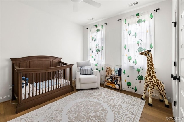 bedroom featuring a crib, a ceiling fan, visible vents, and wood finished floors