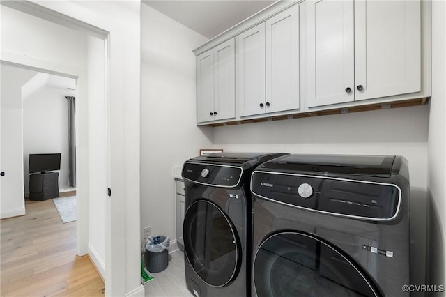 laundry room with light wood finished floors, washing machine and clothes dryer, cabinet space, and baseboards