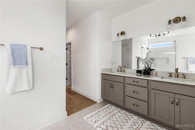 bathroom featuring double vanity, baseboards, walk in shower, and a sink