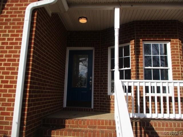 doorway to property with covered porch and brick siding