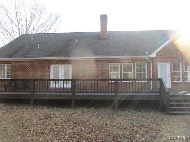 back of house featuring french doors, a chimney, roof with shingles, a wooden deck, and brick siding