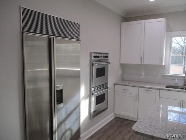 kitchen featuring stainless steel appliances, dark wood-style flooring, white cabinetry, ornamental molding, and light stone countertops