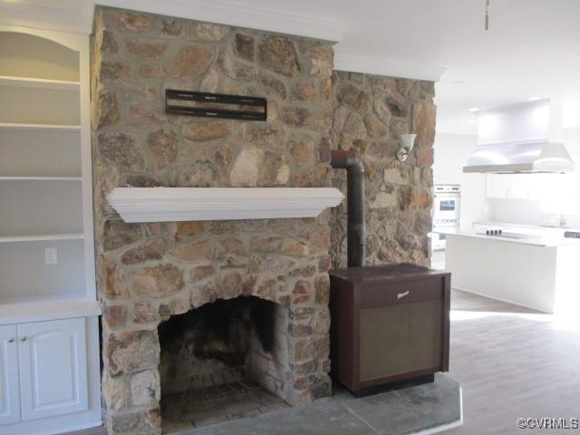 interior details with wood finished floors, a stone fireplace, island exhaust hood, and ornamental molding