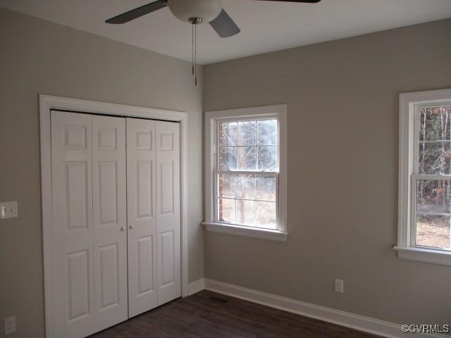 unfurnished bedroom featuring dark wood-style floors, multiple windows, a closet, and baseboards