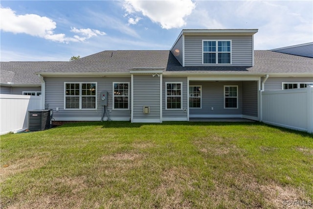 back of property with central air condition unit, fence, a lawn, and roof with shingles