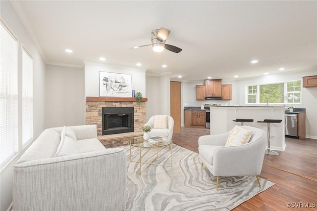 living area featuring recessed lighting, crown molding, wood finished floors, and a stone fireplace