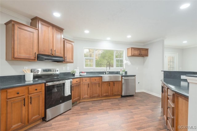 kitchen with under cabinet range hood, stainless steel appliances, a sink, brown cabinets, and dark countertops