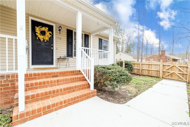 doorway to property with a porch, a gate, brick siding, and fence