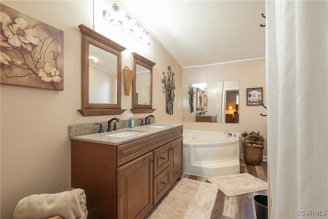 full bathroom featuring double vanity, a textured ceiling, a garden tub, and a sink