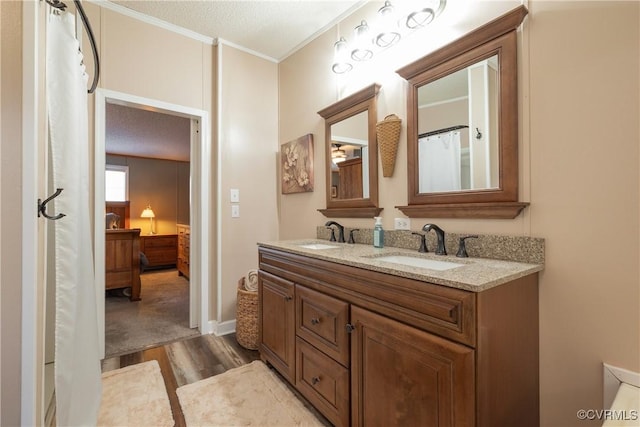 ensuite bathroom featuring double vanity, wood finished floors, crown molding, and a sink