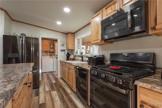 kitchen featuring stainless steel fridge with ice dispenser, a sink, gas range oven, dishwasher, and washing machine and dryer