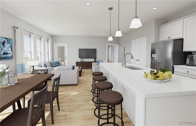 kitchen with a sink, white cabinetry, light wood-style floors, stainless steel refrigerator with ice dispenser, and an island with sink