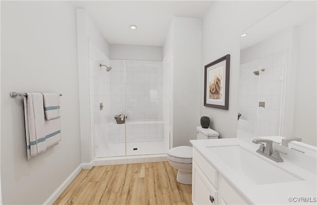 bathroom featuring toilet, a tile shower, vanity, wood finished floors, and baseboards