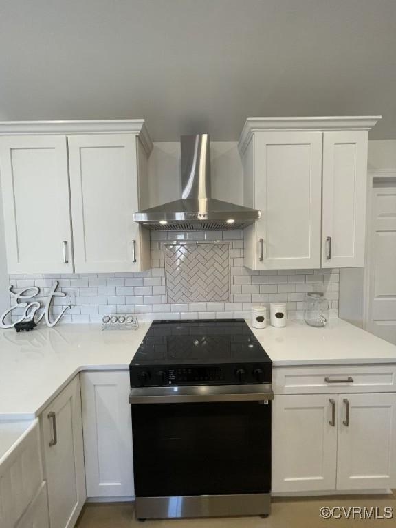 kitchen with black electric range, tasteful backsplash, light countertops, white cabinetry, and wall chimney exhaust hood