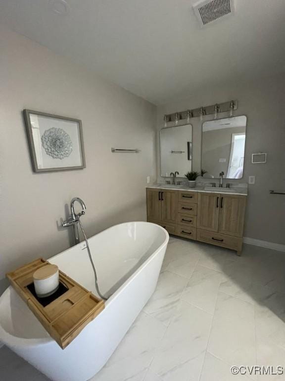 full bath featuring marble finish floor, double vanity, visible vents, a sink, and a freestanding tub