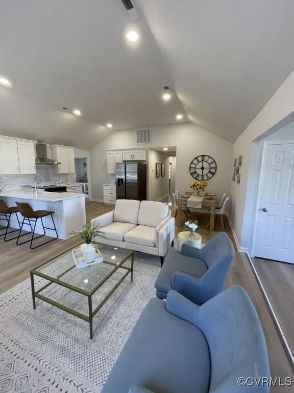 living area with light wood-type flooring, lofted ceiling, visible vents, and recessed lighting