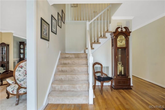 stairs with visible vents, wood finished floors, baseboards, and ornamental molding