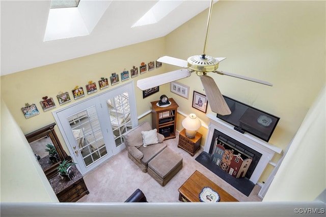 living room with carpet, ceiling fan, a fireplace, a skylight, and high vaulted ceiling