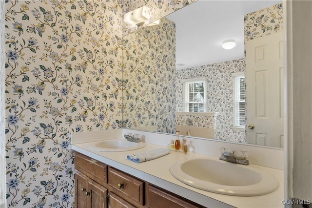 bathroom featuring wallpapered walls, double vanity, and a sink