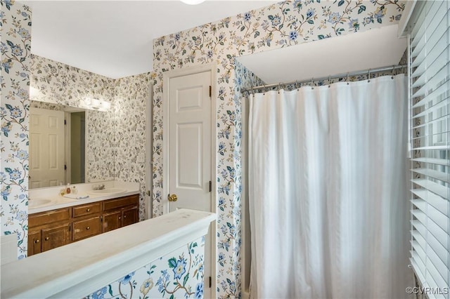 full bath featuring wallpapered walls, double vanity, a shower with curtain, and a sink