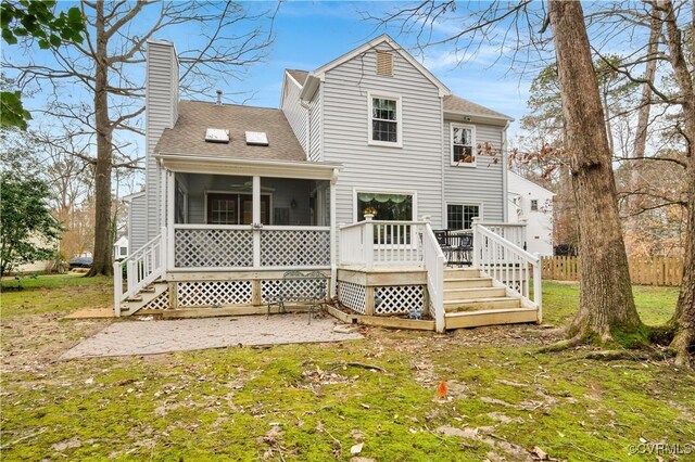 rear view of house featuring a lawn, roof with shingles, a sunroom, a wooden deck, and a chimney