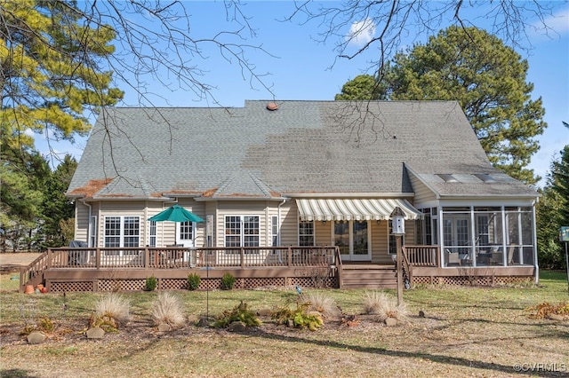 rear view of property with a shingled roof, a wooden deck, a sunroom, and a lawn